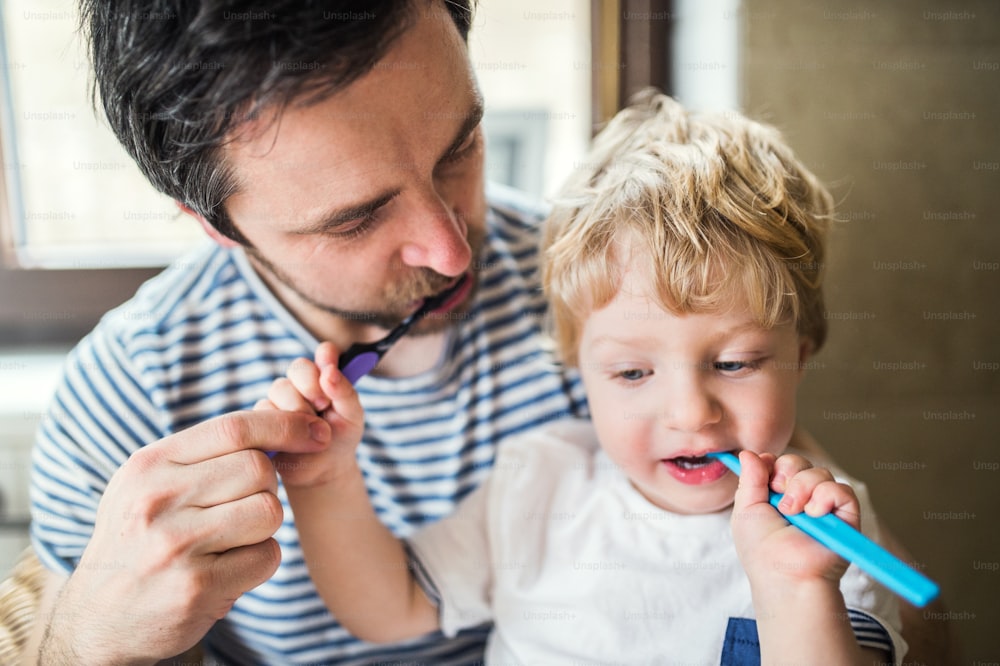 Father brushing his teeth with a toddler boy at home. Paternity leave.