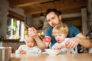 Father feeding two toddlers at home. Paternity leave.