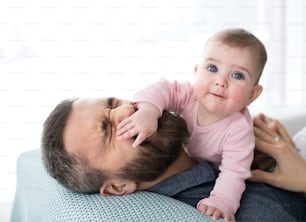Mature father playing with happy baby daughter sitting indoors, having fun.