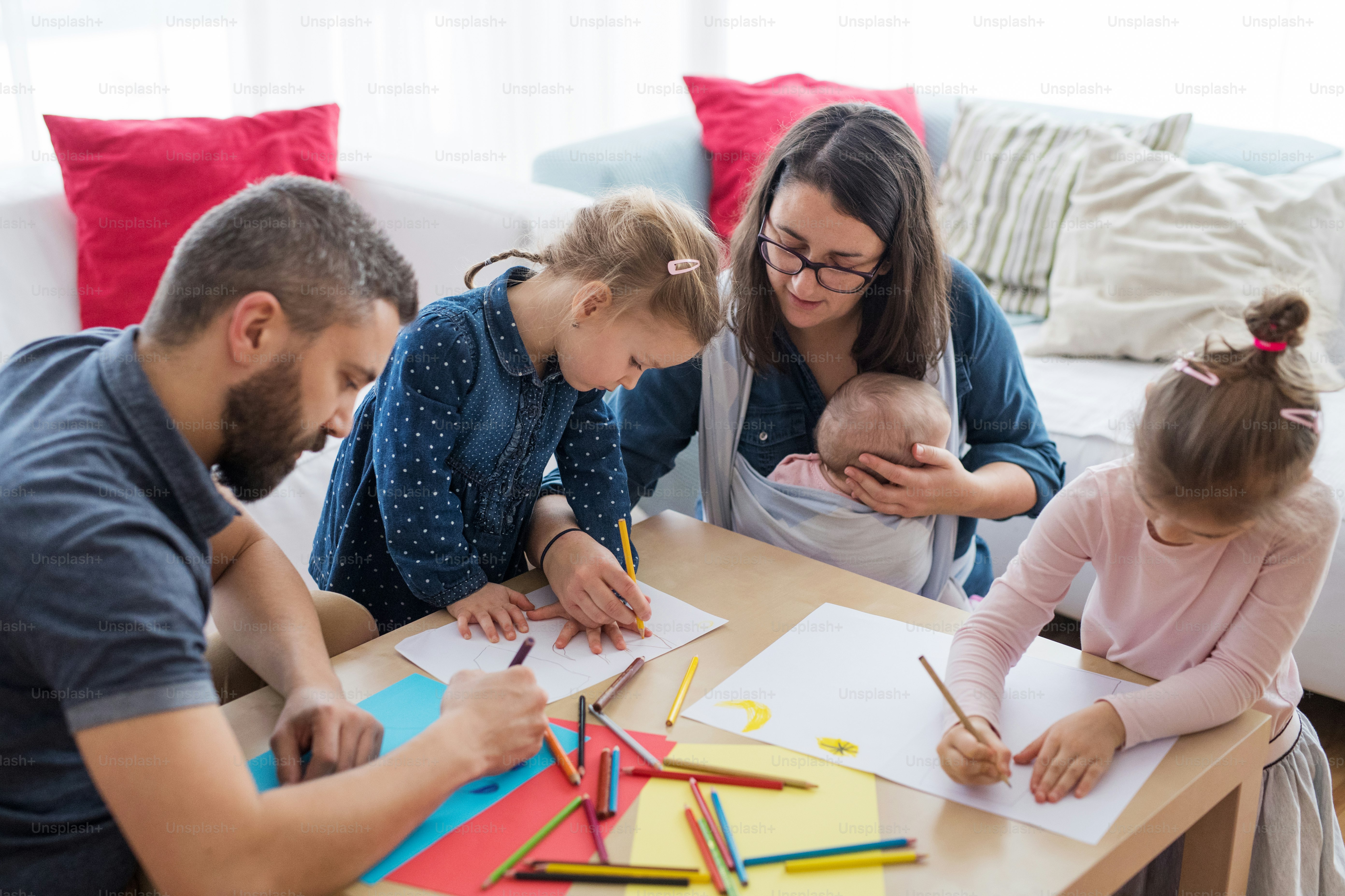 A portrait of happy young family with small children sitting on floor around coffee table indoors, drawing.