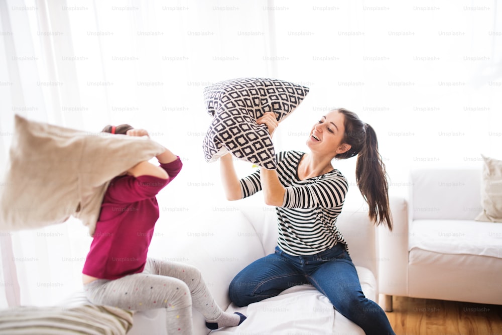 Young mother with a small girl at home, playing. A family having a pillow fight.