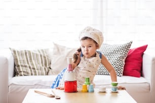 A cute small girl with apron and a hat playing at home.