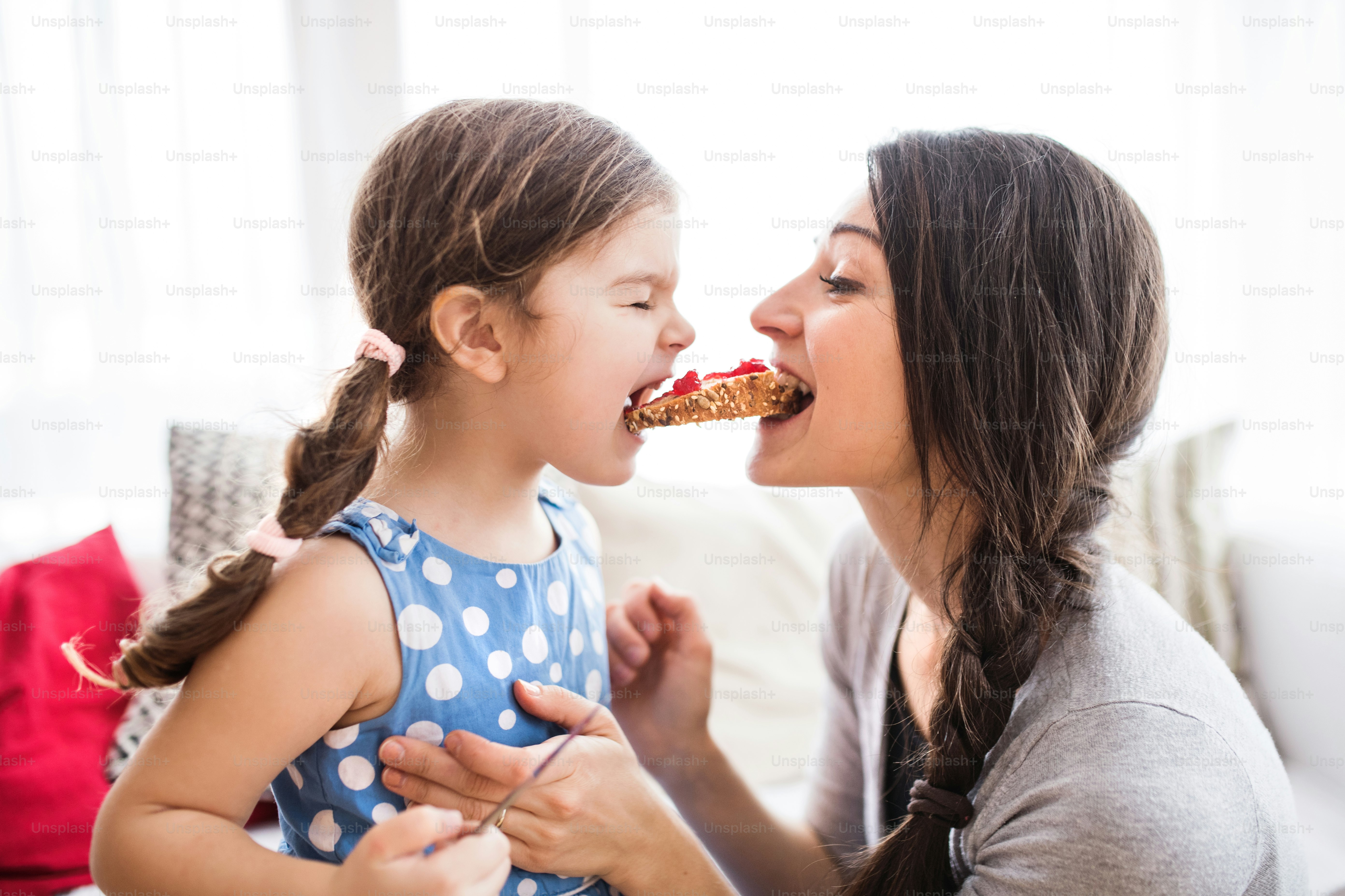 Giovane madre con una bambina a casa, divertendosi a mangiare.