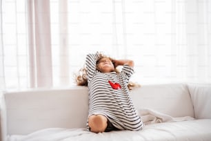 Uma menina pequena e feliz bonita em camiseta listrada em casa se divertindo.