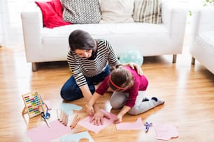 Giovane madre con una bambina a casa, seduta sul pavimento e disegnando.