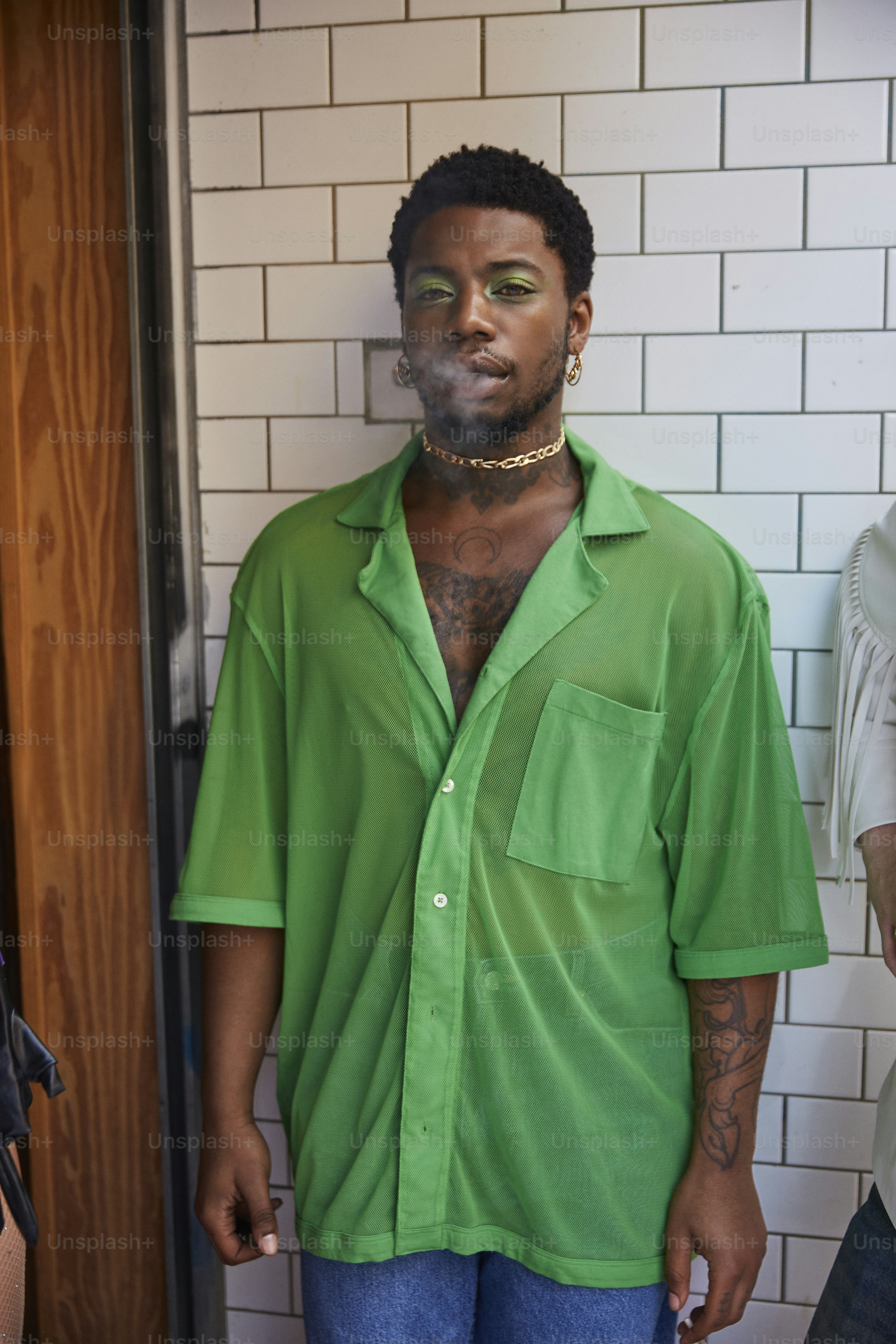a man in a green shirt standing in front of a white brick wall
