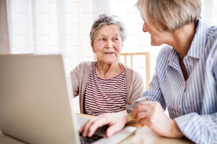 Mujer mayor irreconocible con su madre con computadora portátil en casa. Concepto de familia y generaciones.