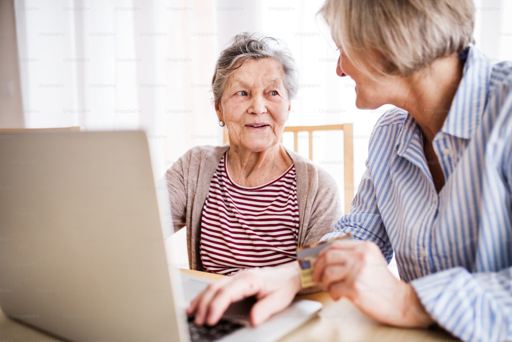 Donna anziana irriconoscibile con sua madre con il computer portatile a casa. Concetto di famiglia e generazioni.