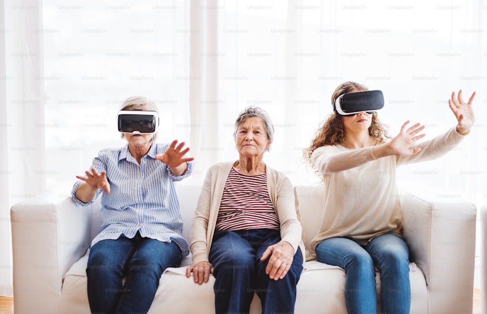 A teenage girl, her mother and grandmother with VR goggles at home. Family and generations concept.