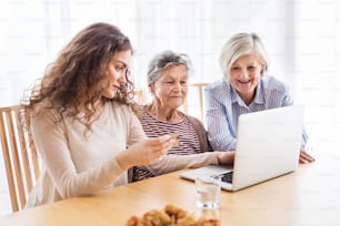 Une adolescente, sa mère et sa grand-mère avec un ordinateur portable à la maison. Concept de famille et de générations.