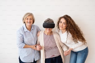Uma adolescente, sua mãe e avó com óculos de realidade virtual em casa. Conceito de família e gerações.