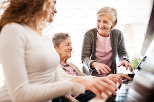 A teenage girl with mother and grandmother playing the piano at home. Family and generations concept.