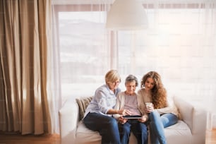 A teenage girl, her mother and grandmother with tablet and smartphones at home. Family and generations concept.