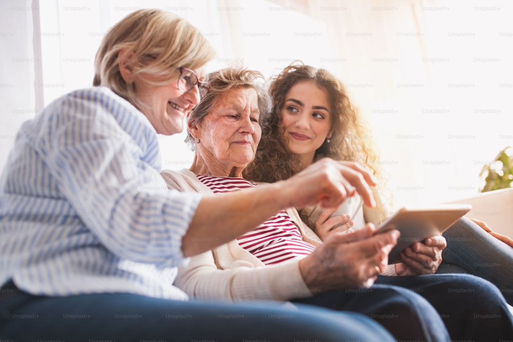 Una ragazza adolescente, sua madre e sua nonna con tablet e smartphone a casa. Concetto di famiglia e generazioni.