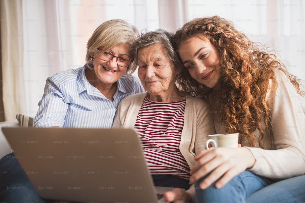 A teenage girl, her mother and grandmother with laptop at home. Family and generations concept.