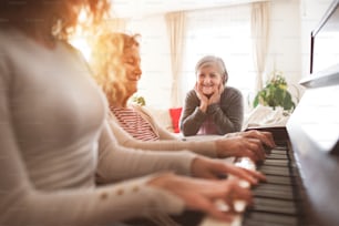An unrecognizable teenage girl with mother and grandmother playing the piano at home. Family and generations concept.