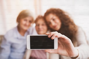 A teenage girl, her mother and grandmother with smartphone at home. Family and generations concept. Copy space.