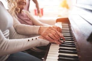 Uma adolescente irreconhecível com a avó tocando piano em casa. Conceito de família e gerações.