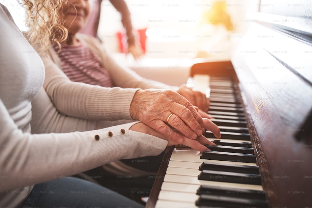 An unrecognizable teenage girl with grandmother playing the piano at home. Family and generations concept.