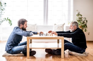 Hipster son and his senior father at home, playing chess. Two generations indoors.