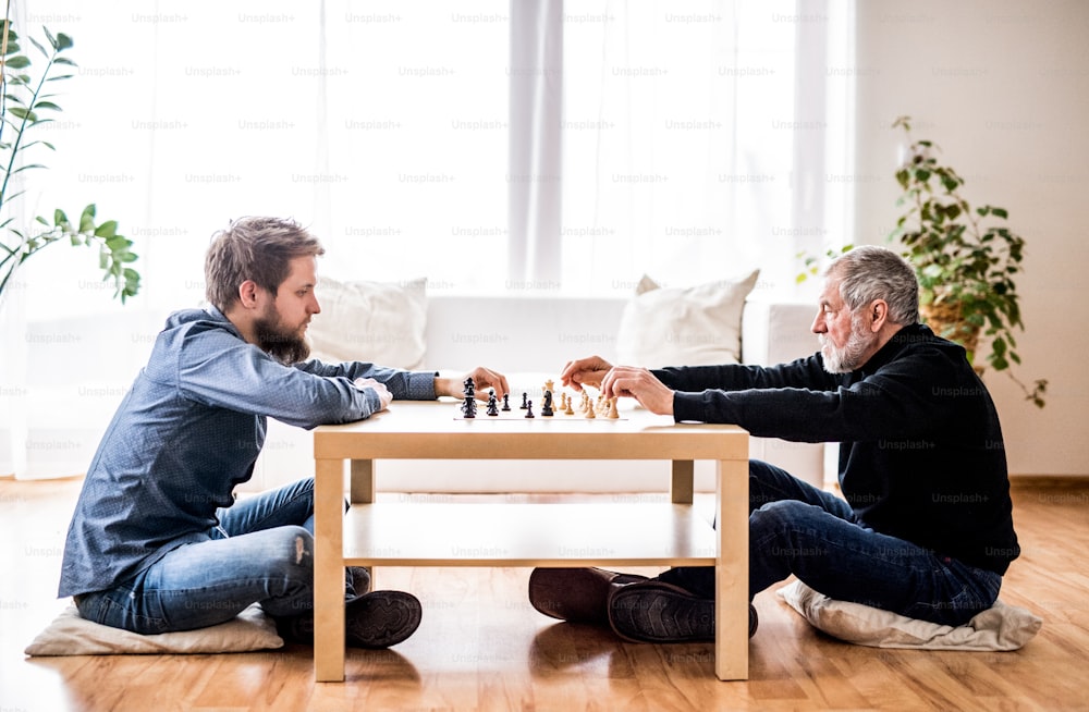 Hipster son and his senior father at home, playing chess. Two generations indoors.