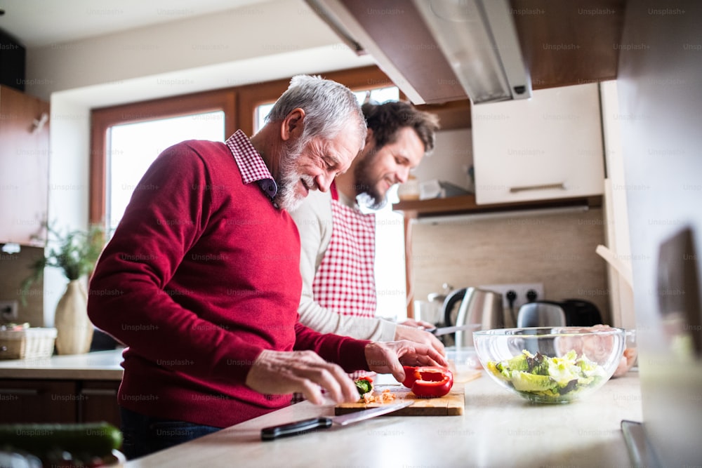 Hijo hipster con su padre mayor cocinando en la cocina. Dos generaciones en interior.