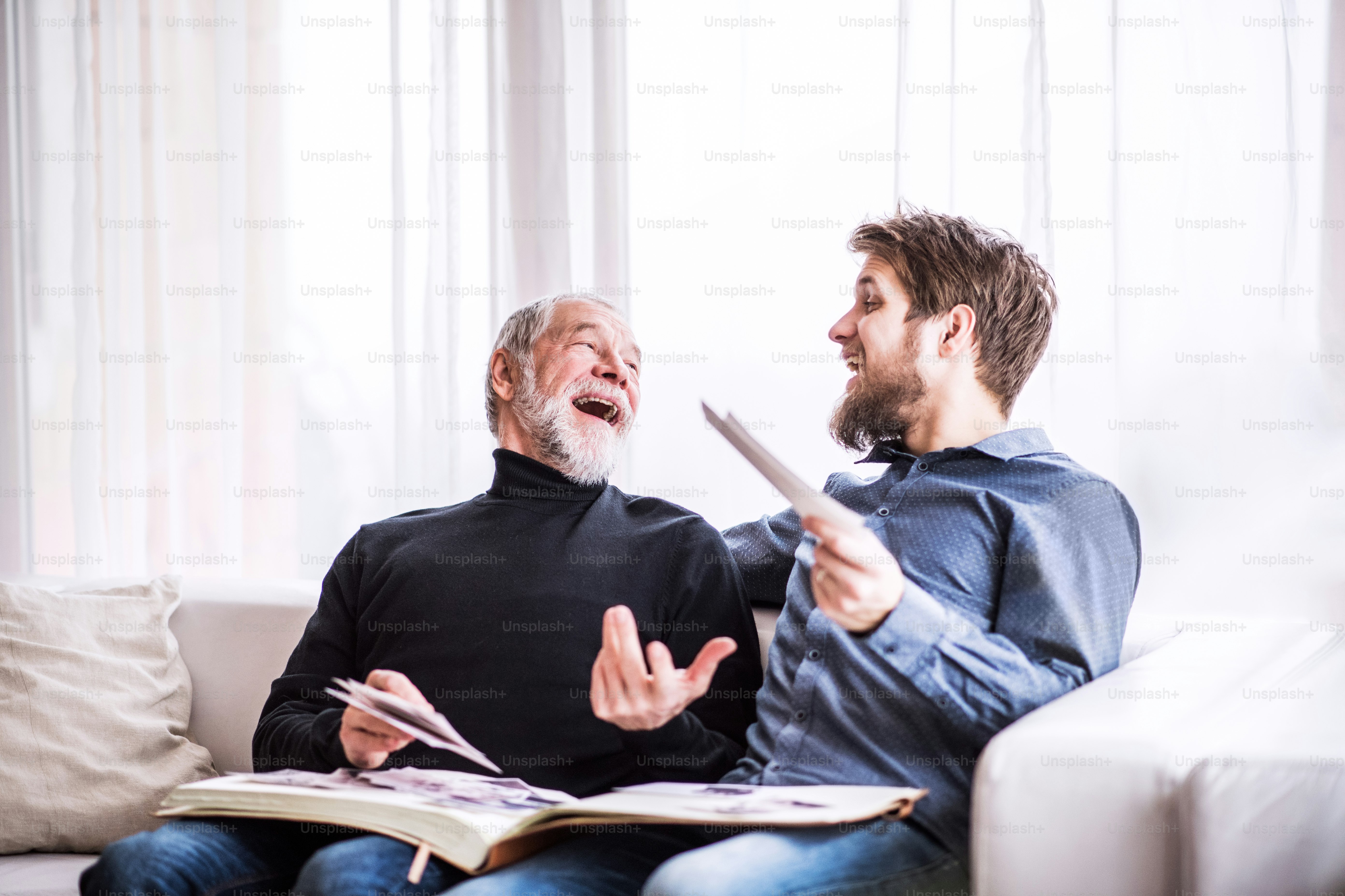Hipster son and his senior father at home, looking at old photographs. Two generations indoors.