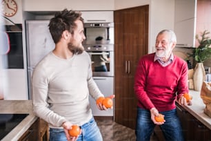 Hipster son with his senior father in the kitchen, juggling. Two generations indoors.