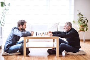 Hipster son and his senior father at home, playing chess. Two generations indoors.