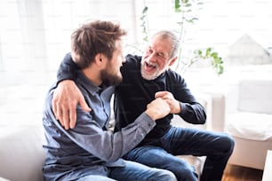 Hipster son with his senior father at home. Two generations indoors, having fun.