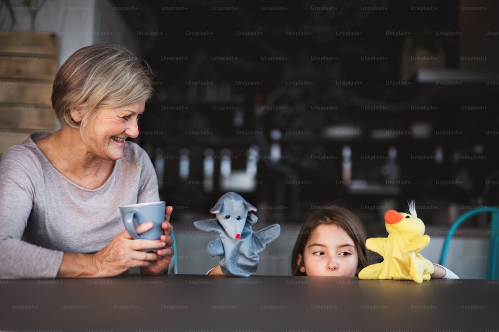 Una niña pequeña y su abuela con tableta en casa, jugando. Concepto de familia y generaciones.