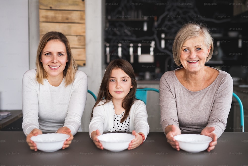 A small girl with her mother and grandmother at home, holding bowls. Family and generations concept.