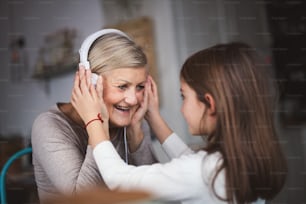 A small girl and her grandmother with headphones at home. Family and generations concept.