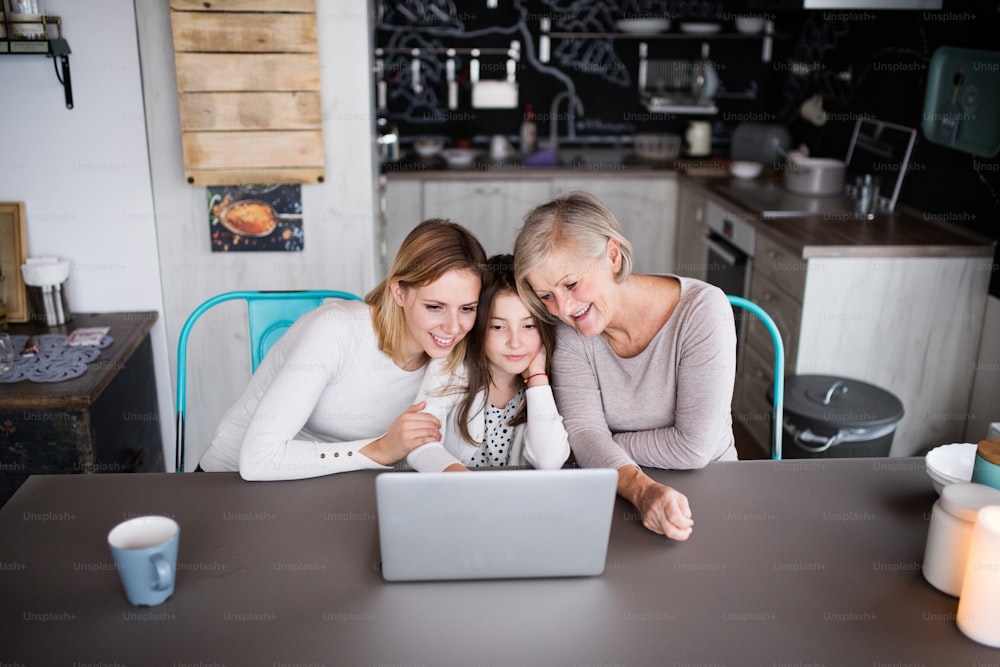 Una niña pequeña con computadora portátil y su madre y abuela en casa. Concepto de familia y generaciones.