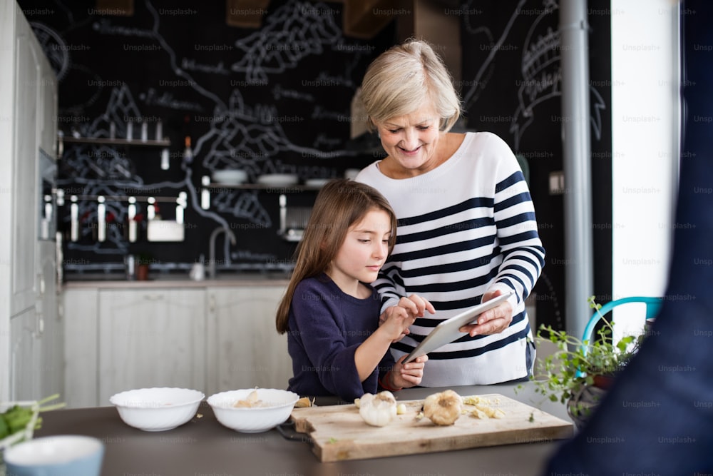 A small girl and her grandmother with a tablet at home, cooking. Family and generations concept.