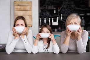 A small girl with her mother and grandmother at home, holding bowls. Family and generations concept.