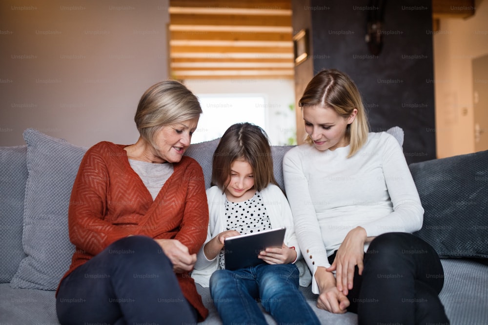 A small girl with tablet and her mother and grandmother at home. Family and generations concept.