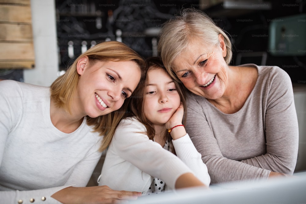 Una bambina con il computer portatile e sua madre e sua nonna a casa. Concetto di famiglia e generazioni.