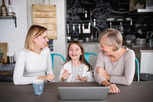 Uma menina pequena com laptop e sua mãe e avó em casa. Conceito de família e gerações.