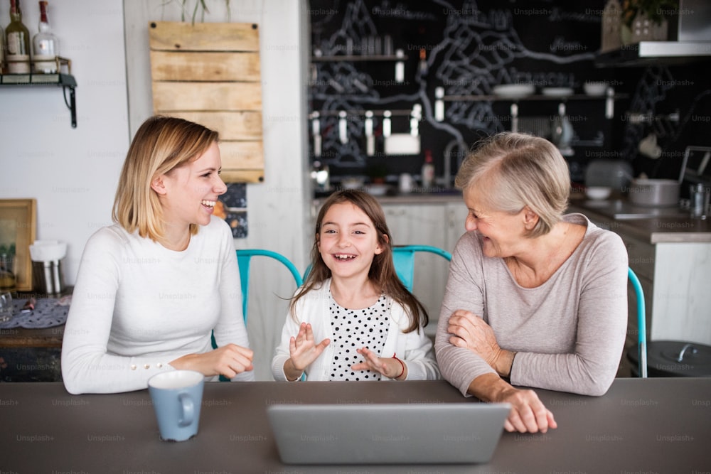 A small girl with laptop and her mother and grandmother at home. Family and generations concept.