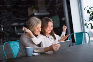 Une petite fille et sa grand-mère avec une tablette à la maison. Concept de famille et de générations.