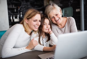 Una bambina con il computer portatile e sua madre e sua nonna a casa. Concetto di famiglia e generazioni.