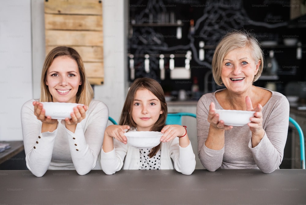 A small girl with her mother and grandmother at home, holding bowls. Family and generations concept.