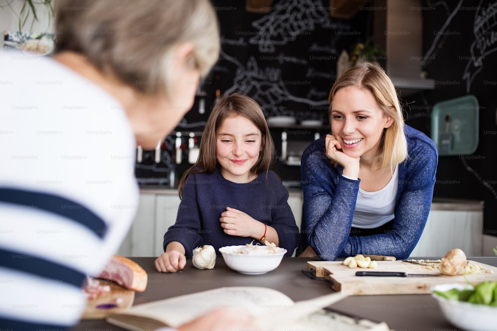 Una niña pequeña con su madre y su abuela en casa, cocinando. Concepto de familia y generaciones.