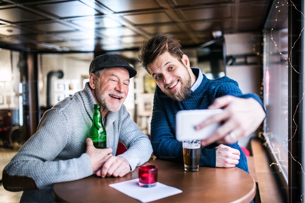 Il padre anziano e il suo giovane figlio bevono birra in un pub. Un giovane che scatta selfie con lo smartphone.