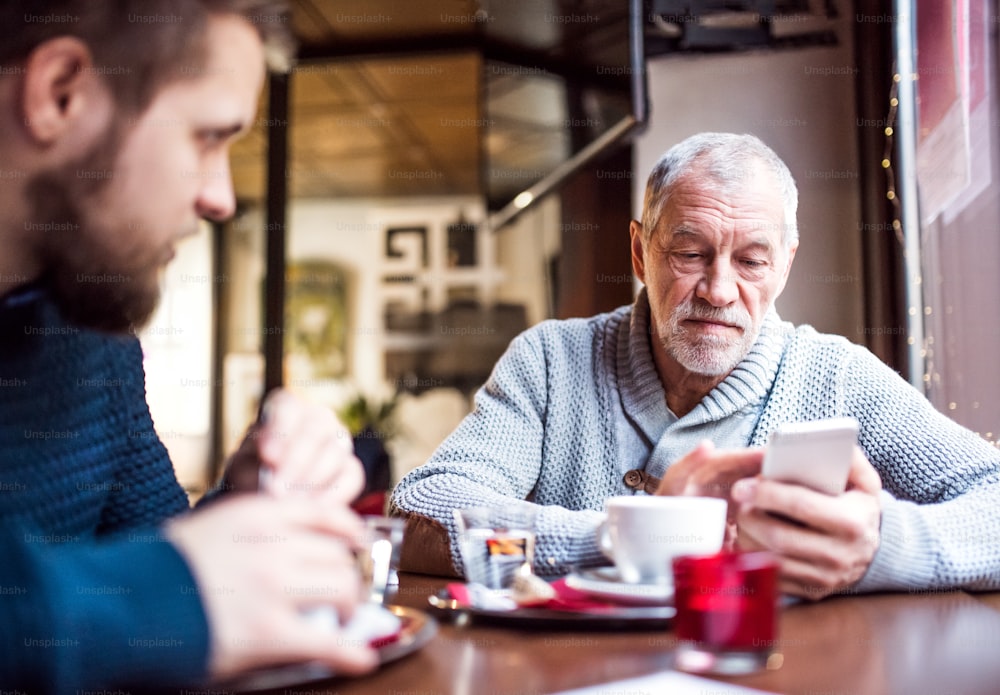 Père aîné avec smartphone et son jeune fils dans un café. Vieil homme faisant de la messagerie texte.