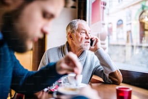 Senior father with smartphone and his young son in a cafe. Old man making a phone call.