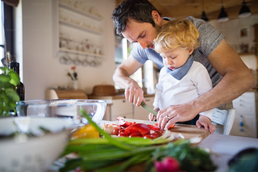 幼児の男の子が料理をする若い父親。息子と野菜サラダを作る男。