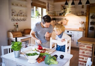 Junger Vater mit einem kleinen Jungen kocht. Ein Mann mit seinem Sohn macht Gemüsesalat.
