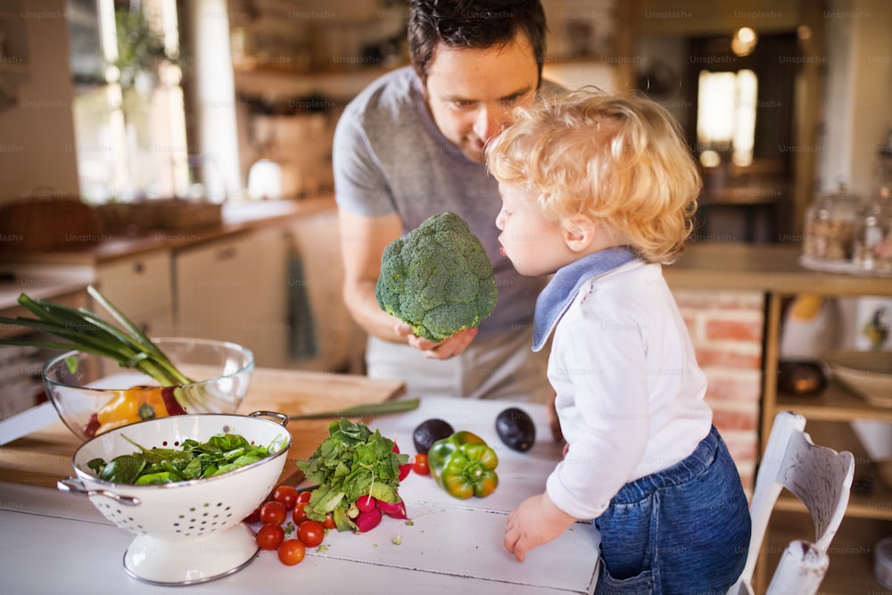 幼児の男の子が料理をする若い父親。息子と野菜サラダを作る男。